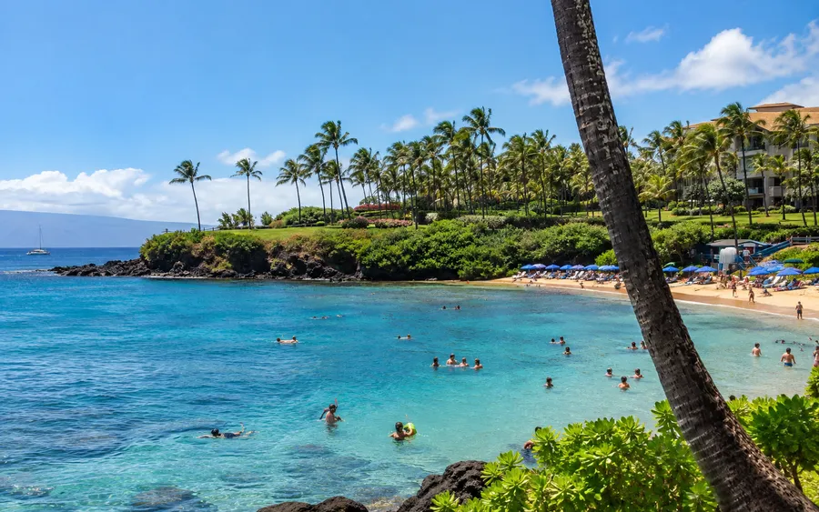 Kapalua Bay in West Maui, swimmers and snorkelers in the calm turquoise water, palm trees and a resort along the shore