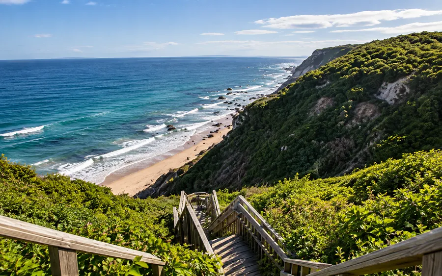 The wooden staircase at Mohegan Bluffs, Block Island, descending green clay cliffs to a sandy beach far below
